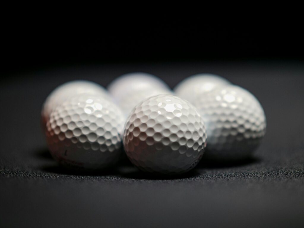 Six white golf balls arranged in close-up on a dark surface, showcasing texture and detail.